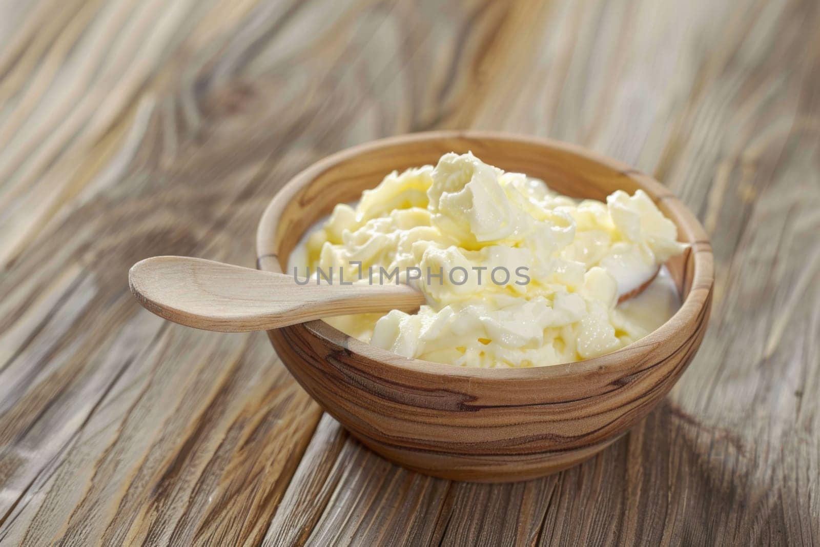 A wooden bowl filled with fluffy whipped cream sits atop a rustic wooden table. The whipped cream is perfectly swirled and looks inviting and delicious.