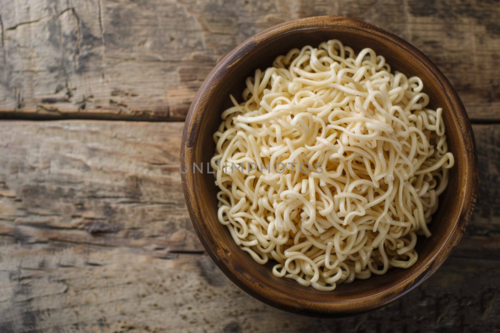 A wooden bowl filled with noodles sits atop a wooden table. The noodles are neatly arranged in the bowl, creating a visually appealing display.