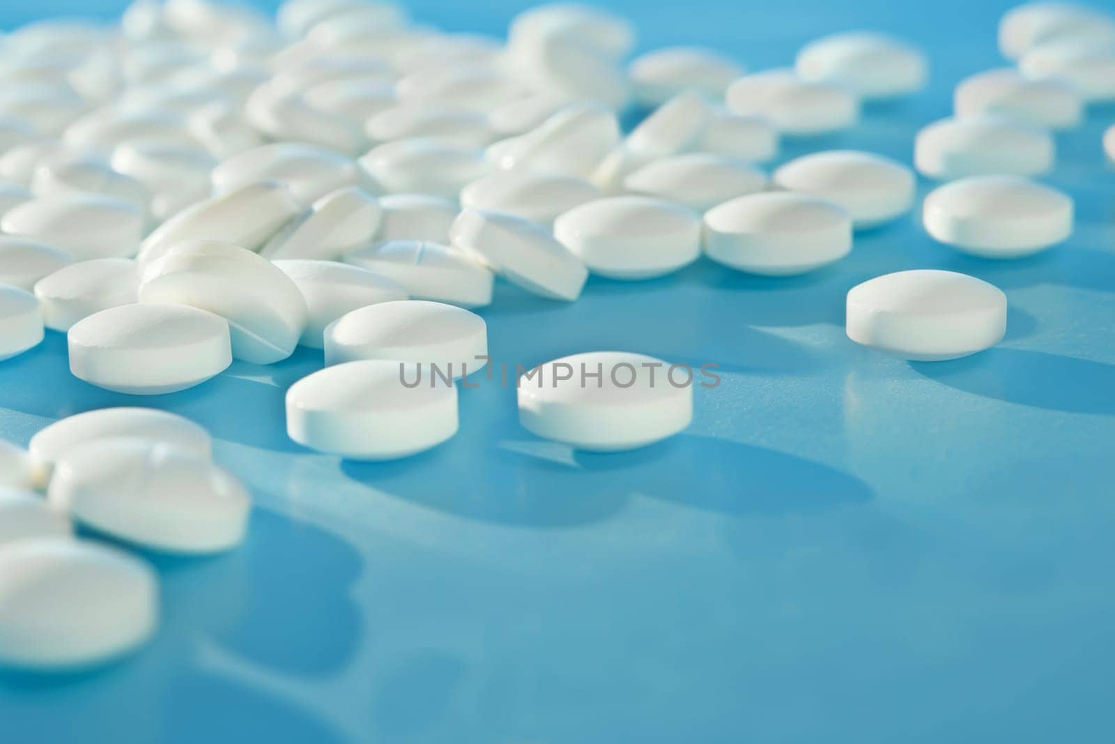 A blue table is covered with numerous white pills, creating a striking visual of medication spread out. The pills are neatly arranged in rows on the surface, presenting a clinical and organized appearance.