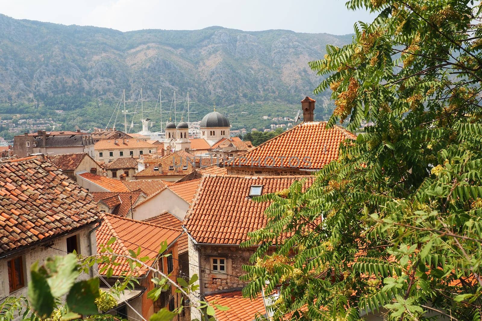 Kotor is a coastal city in Montenegro. Bay of Kotor. Red tiled roofs, mountain and chimneys of a tourist ship. Excursions and tourism. Cathedral of Saint Tryphon. Medieval old towns in the Adriatic.