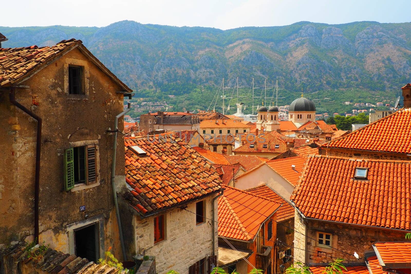 Kotor is a coastal city in Montenegro. Bay of Kotor. Red tiled roofs, mountain and chimneys of a tourist ship. Excursions and tourism. Cathedral of Saint Tryphon. Medieval old towns in the Adriatic.
