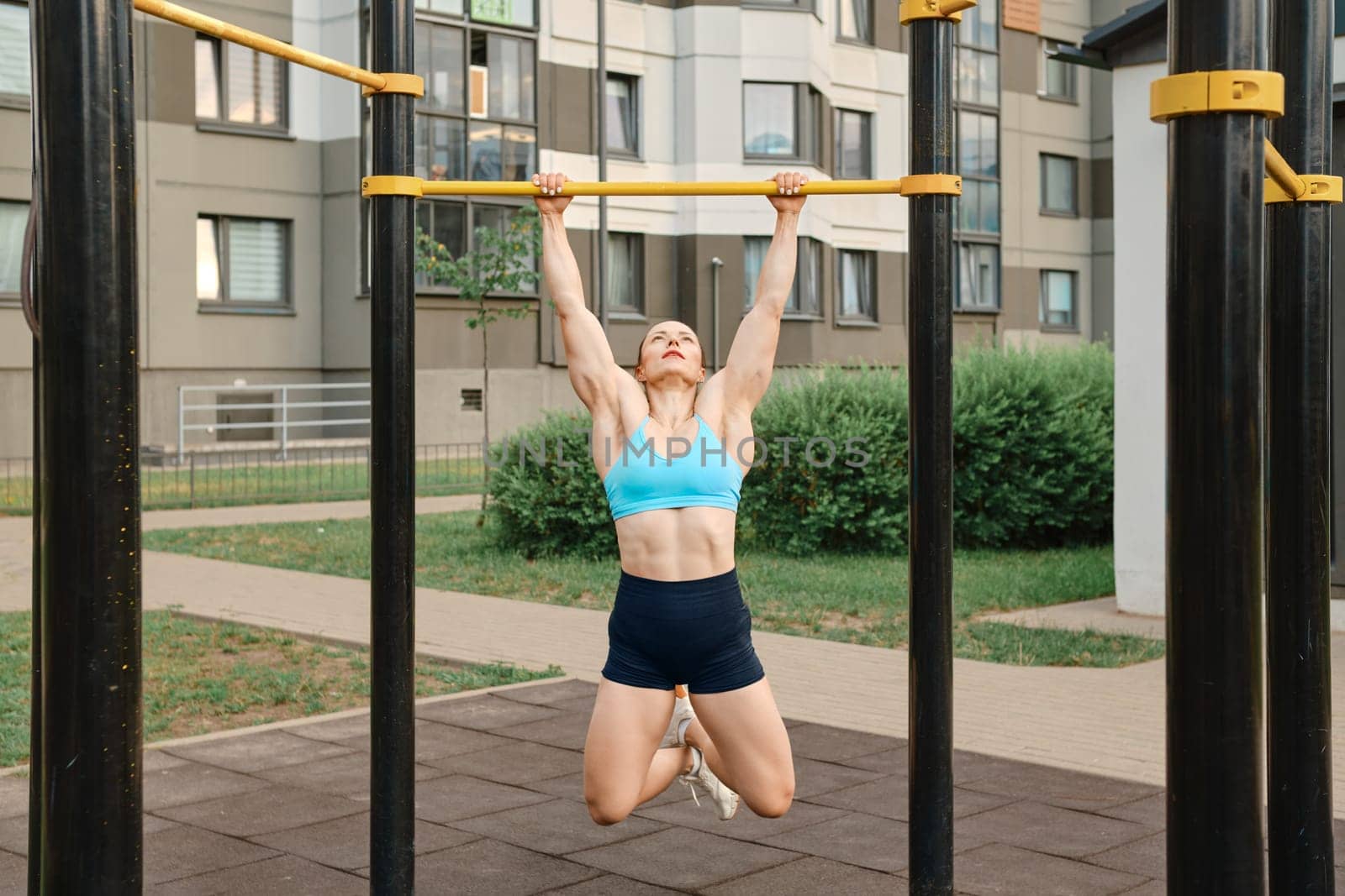 Woman pulls herself up on bar on sports field of residential area