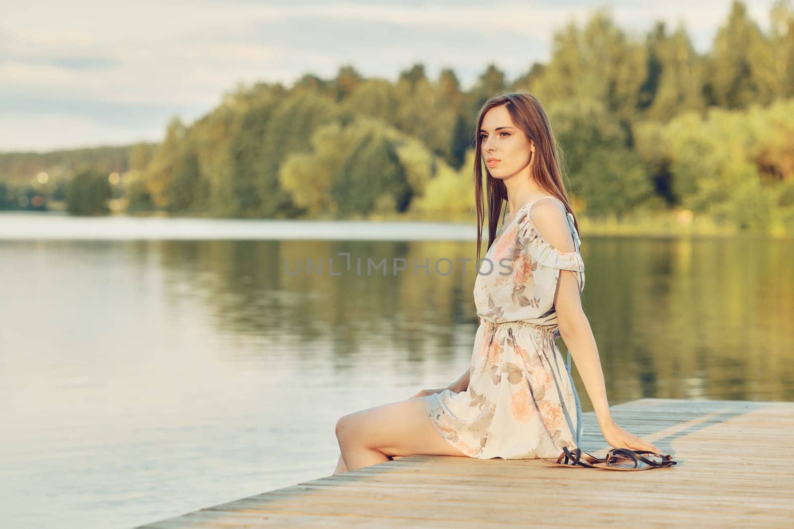 Young woman sits on the pier by the river enjoying beautiful view and fresh air