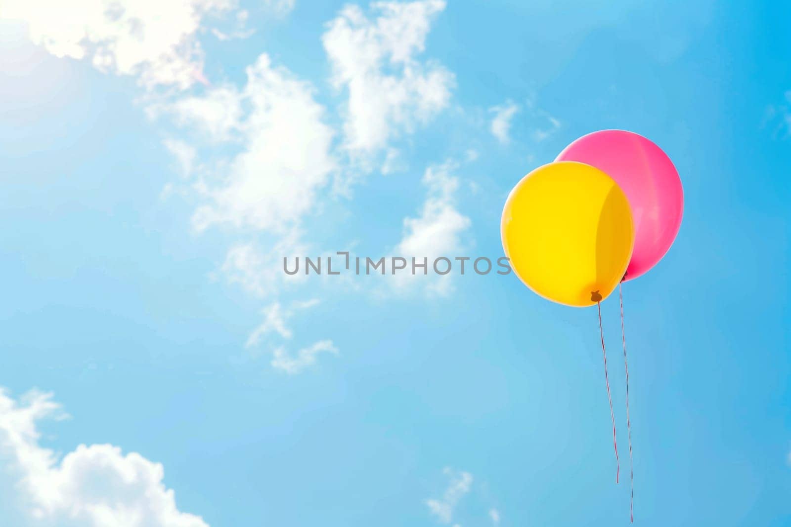 Two colorful balloons are gently floating in the clear blue sky, drifting with the soft breeze as they ascend higher into the atmosphere.
