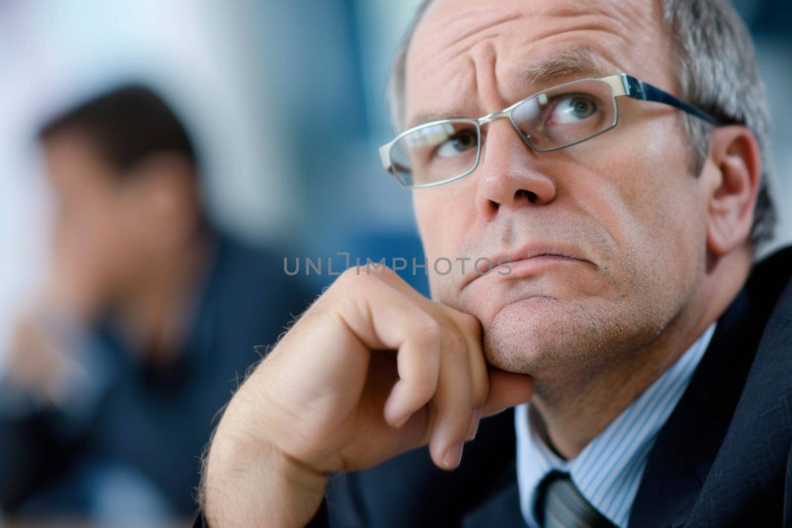 A man dressed in a formal suit and tie is seated at a wooden table, appearing engaged in work or conversation. The setting suggests a professional or corporate environment.