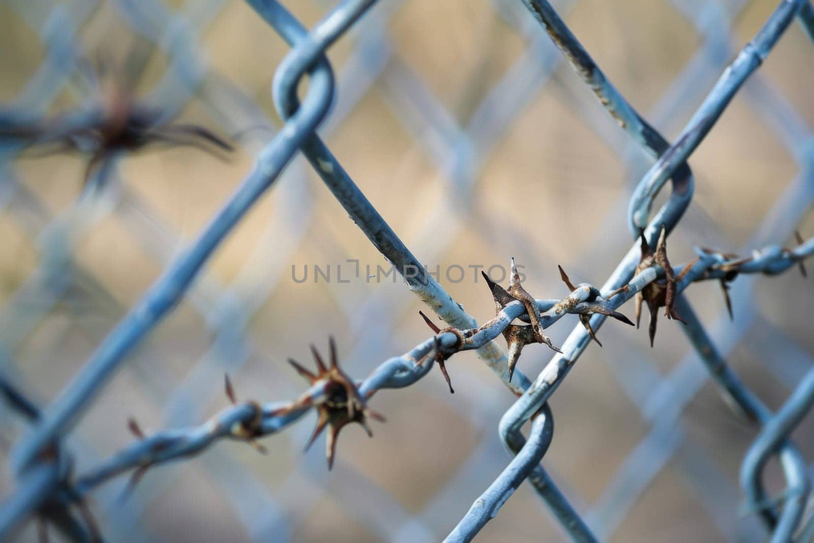 A close-up view of a silver chain link fence, showing its interlocking links and metal construction. The fence is weathered with rust spots and sits against a blurred background.