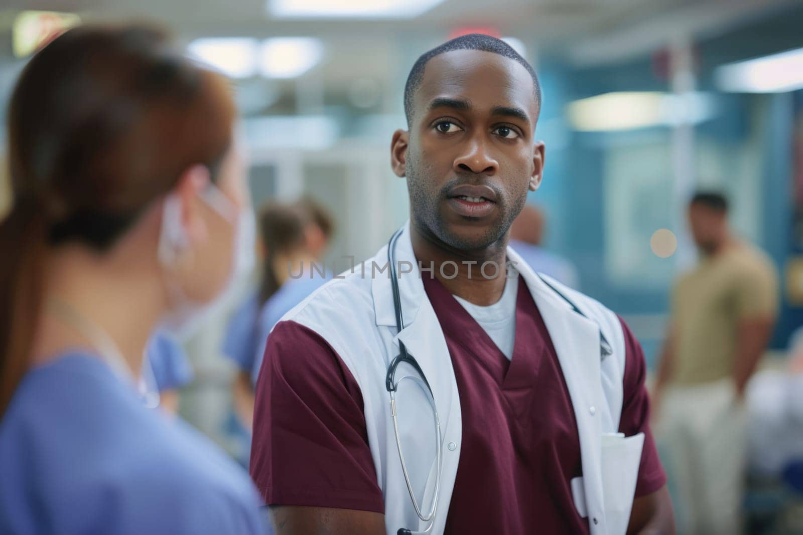 Asian male nurse practitioner wearing maroon scrubs and white coat talking to colleagues at work in hospital. AI Generated.