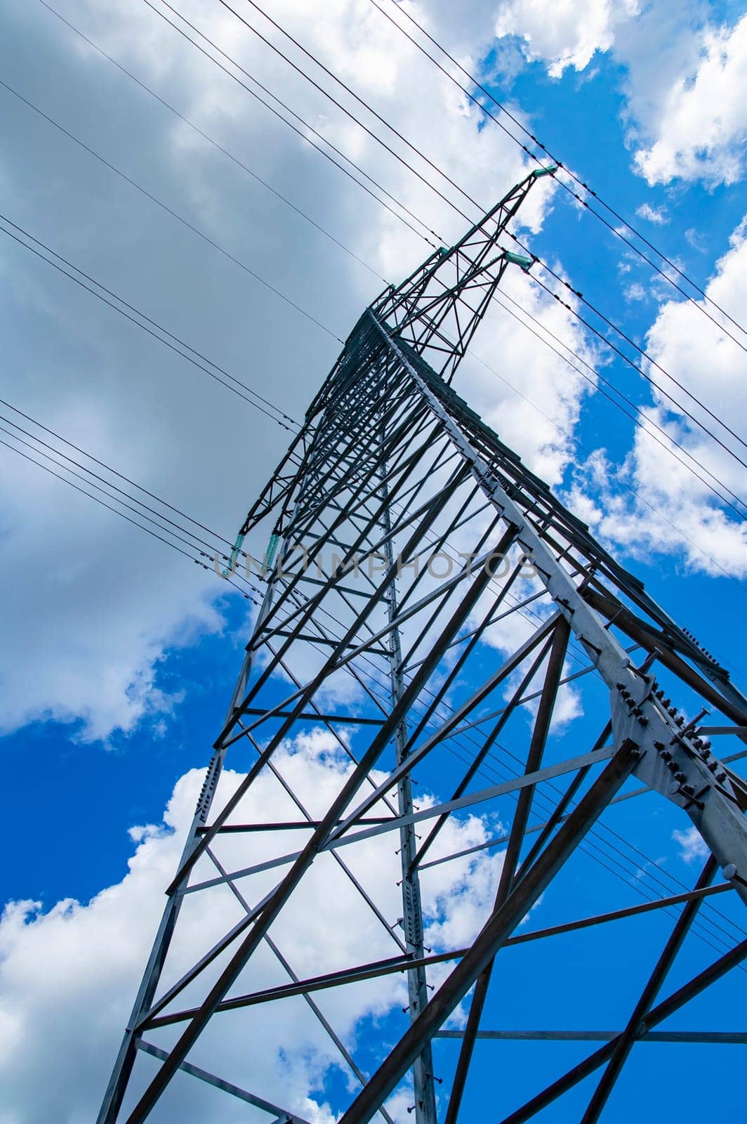 The towers of the power line of energy with cables against the background of nature. High -voltage tower of transmission of electric energy. Industry and nature. Blue sky with white clouds.