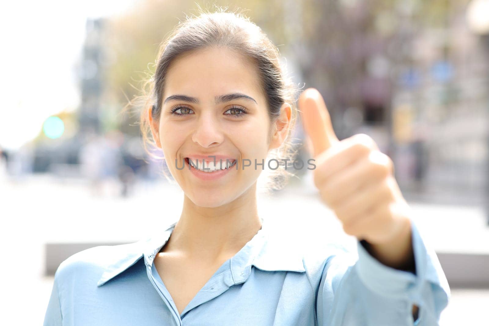 Happy woman gesturing thumbs up at camera in the street