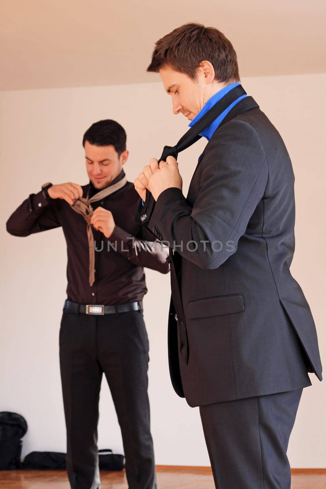 Two men in suits tie their ties
