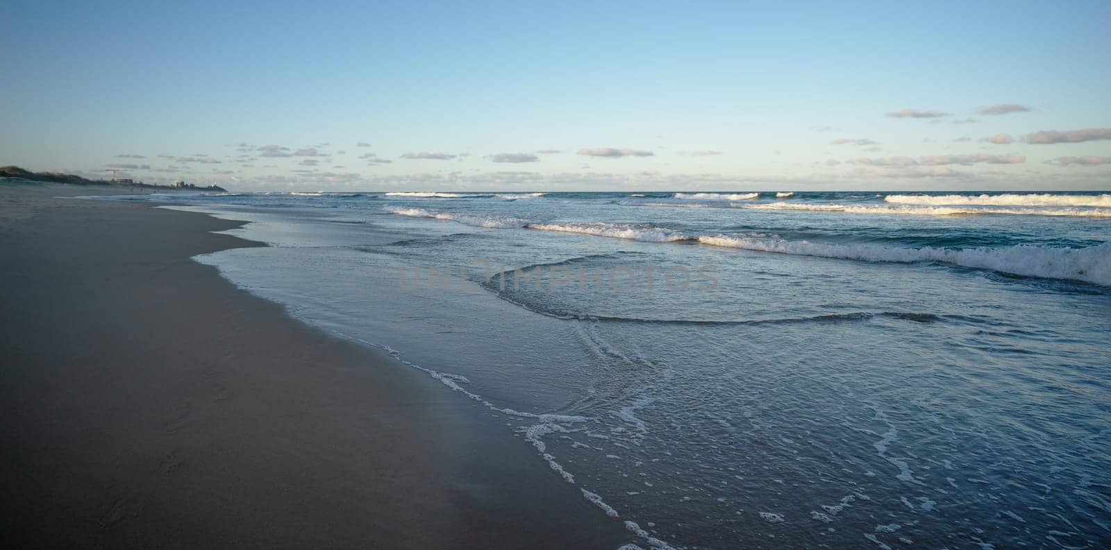 Sunshine Coast, Warana, Kawana showing a beach scene in the late afternoon with dark blue water, white surf waves, wet sand on the shoreline and the setting sun still shining on some of the ocean.