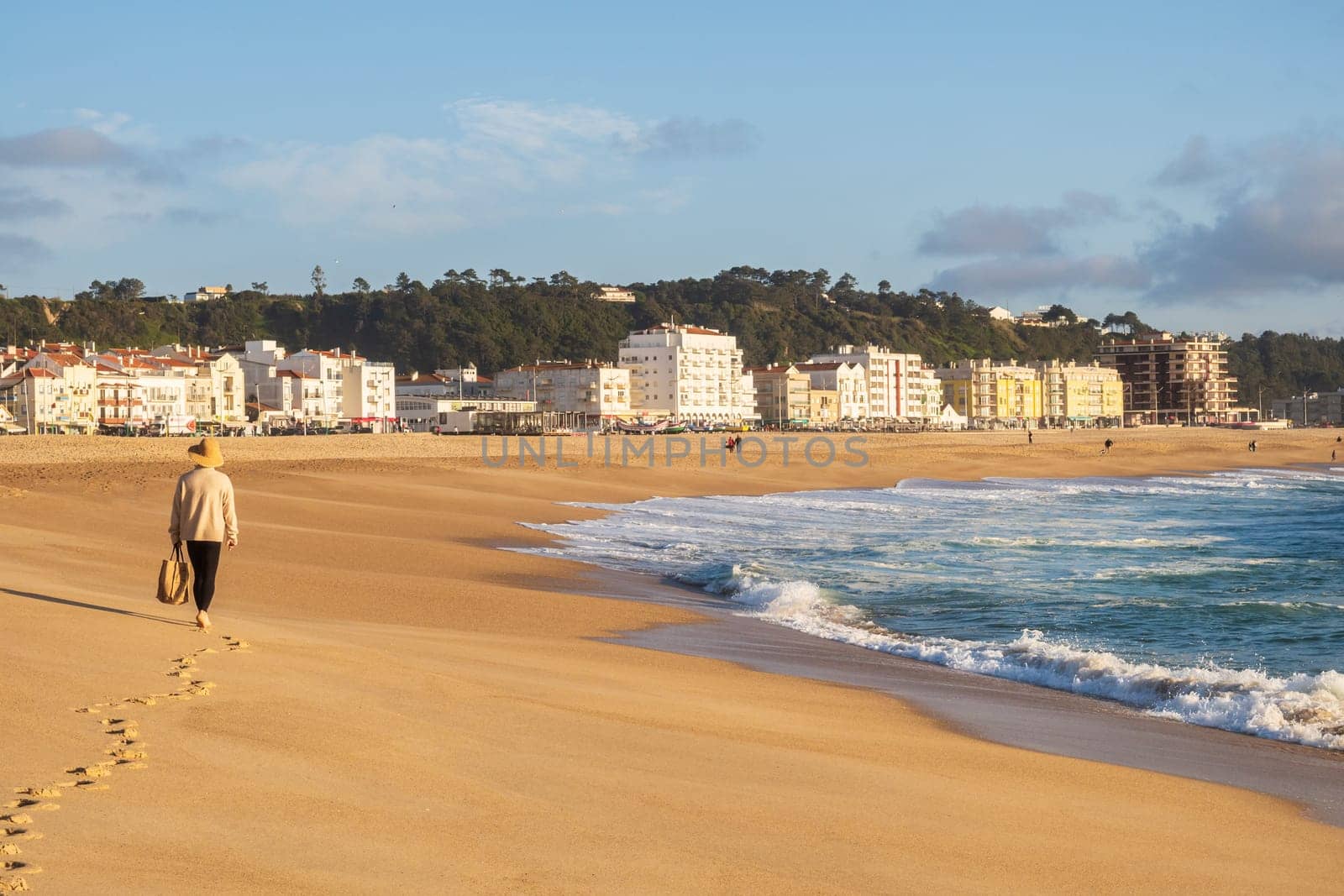 Nazaré, Portugal - Mars 19 2024: Woman walking on the Nazaré Beach and the Atlantic Ocean, Portugal