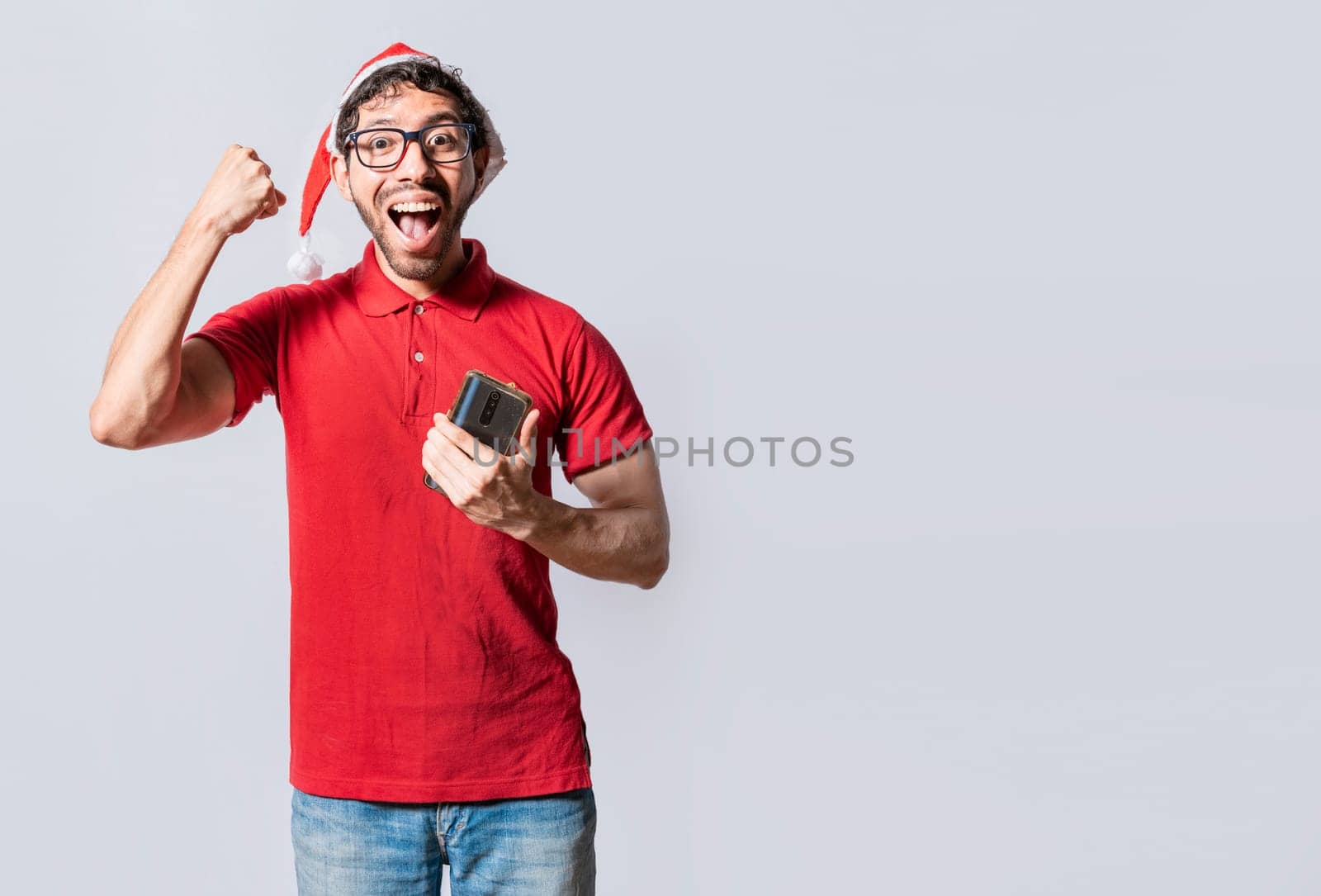 Happy guy in christmas hat holding cellphone celebrating. People with santa hat celebrating a promotion with the cell phone, Happy smiling man in christmas hat holding cellphone celebrating