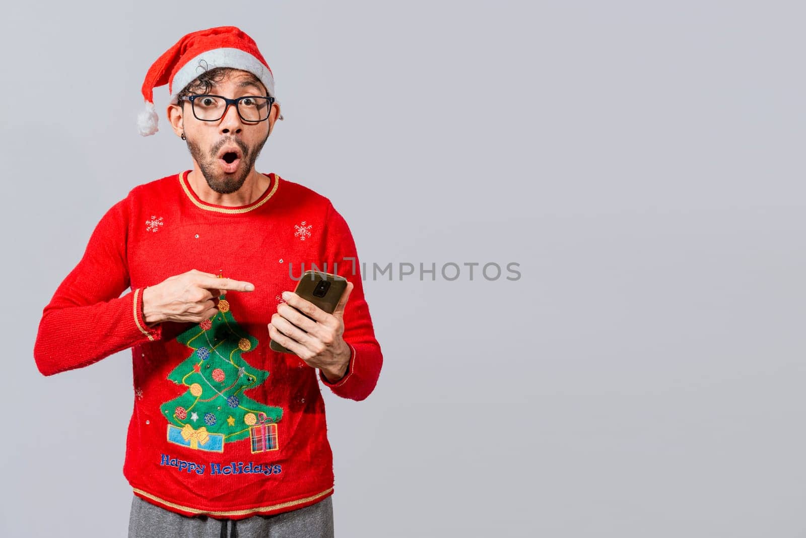 Amazed man pointing at christmas offer online, Guy pointing at christmas promotion on phone. Online Christmas special offers concept, amazed people pointing at a Christmas promotion on phone