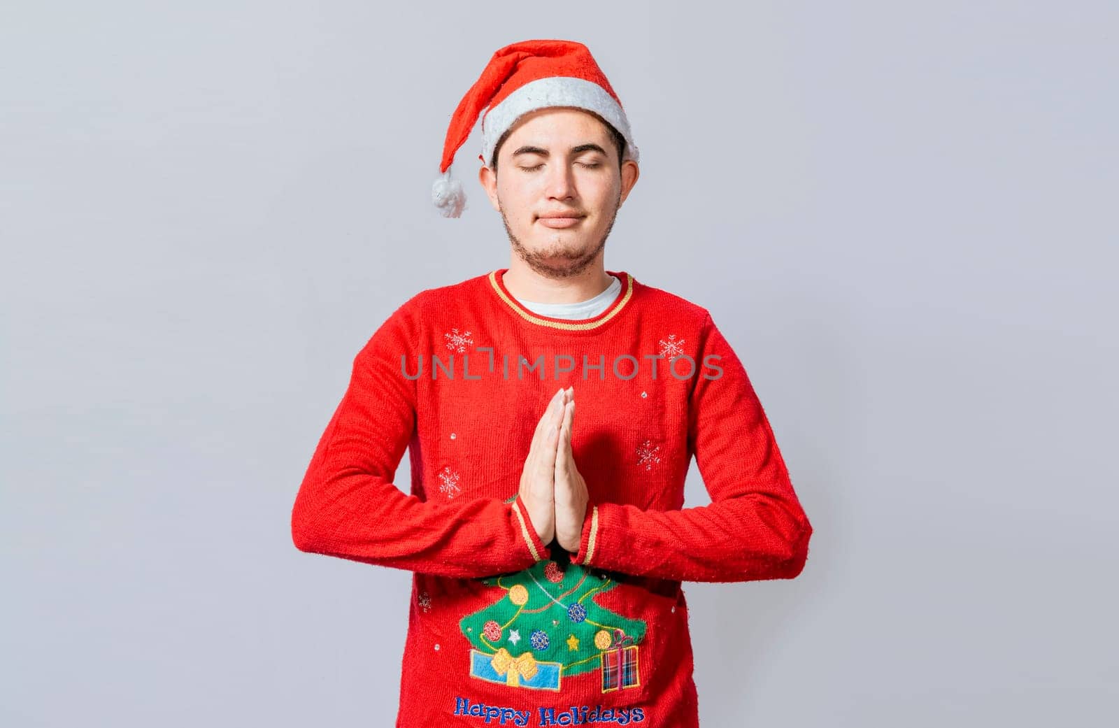 Guy with hands together praying in christmas isolated, concept of person with christmas hat praying and making a wish. Man with christmas hat with praying hands isolated