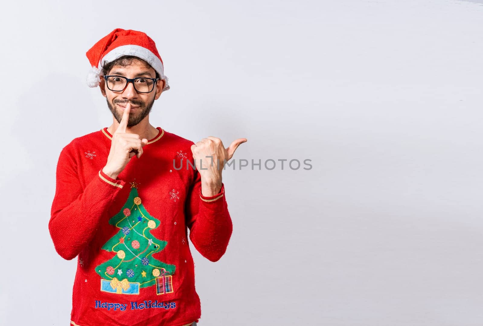 Man in Christmas sweater in silence gesture pointing to the side, Guy in Christmas hat with finger on lips pointing side. Bearded man in christmas hat in silence gesture pointing promo