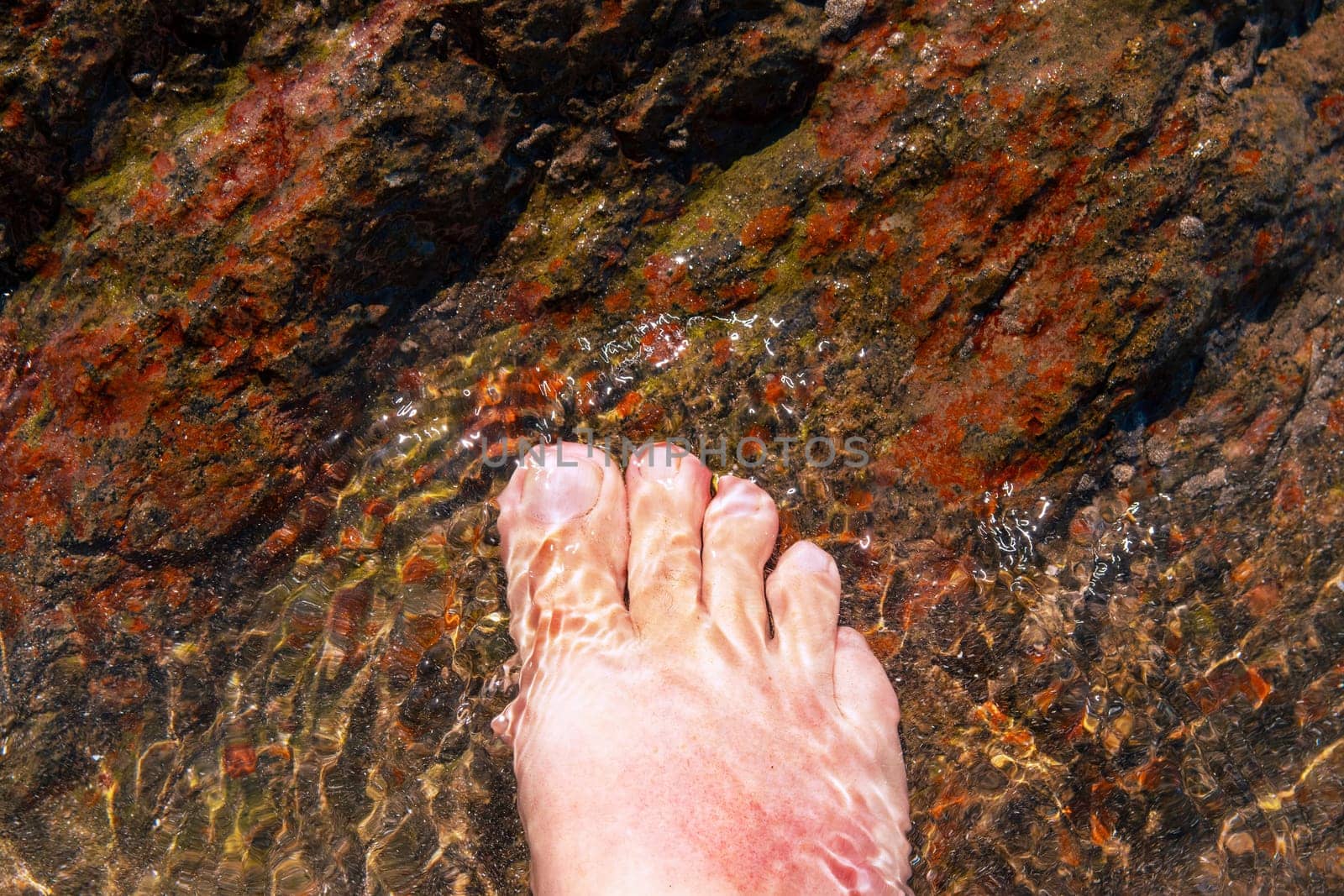 Close-up of a foot under water on stony ground on the beach. Cooling wet for sunburn.