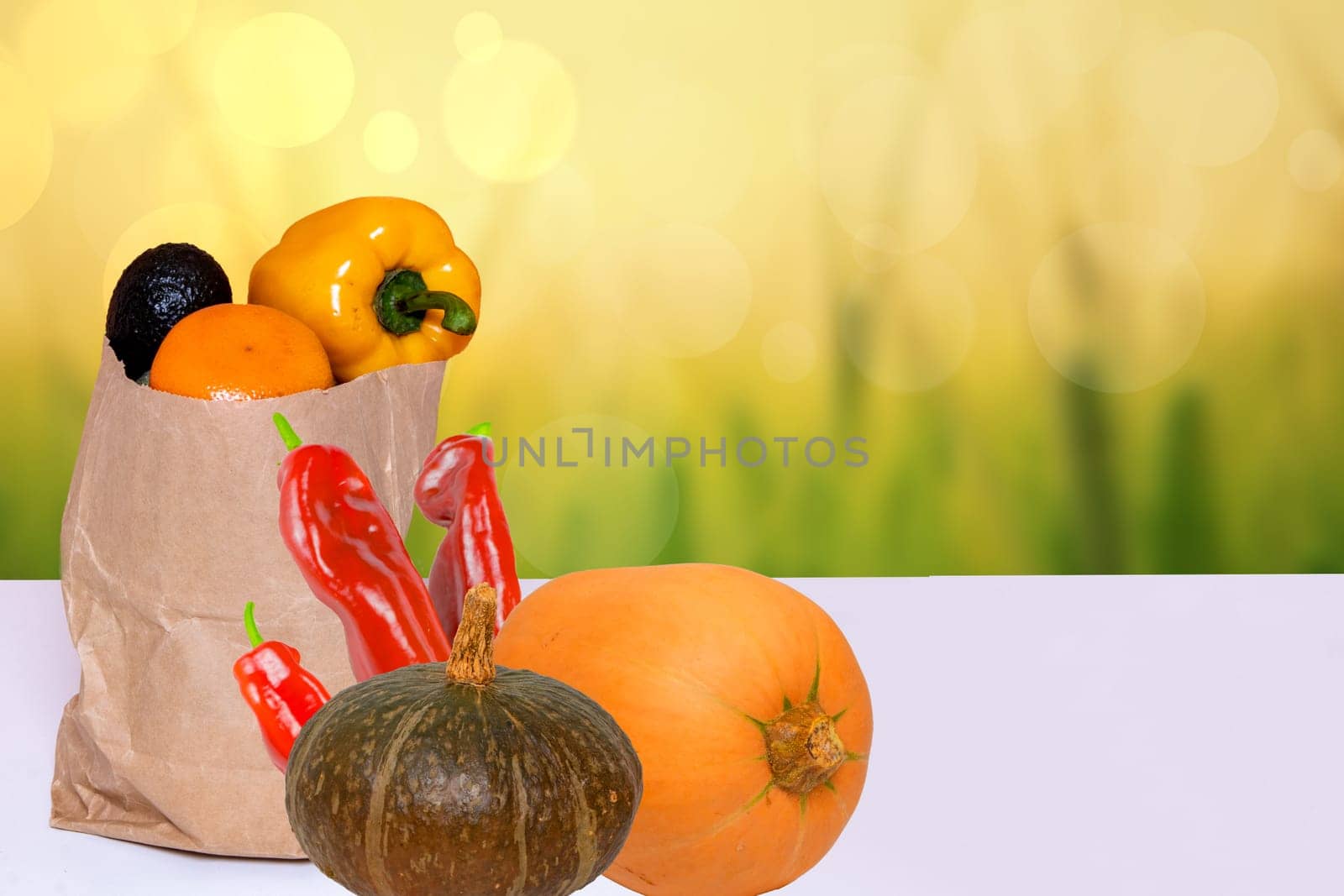 Closeup of a brown paper shopping bag with fresh vegetables and two pumpkins on table over abstract blurred autumn background. Space for food and product display montage. Concept of strengthening the immune system.