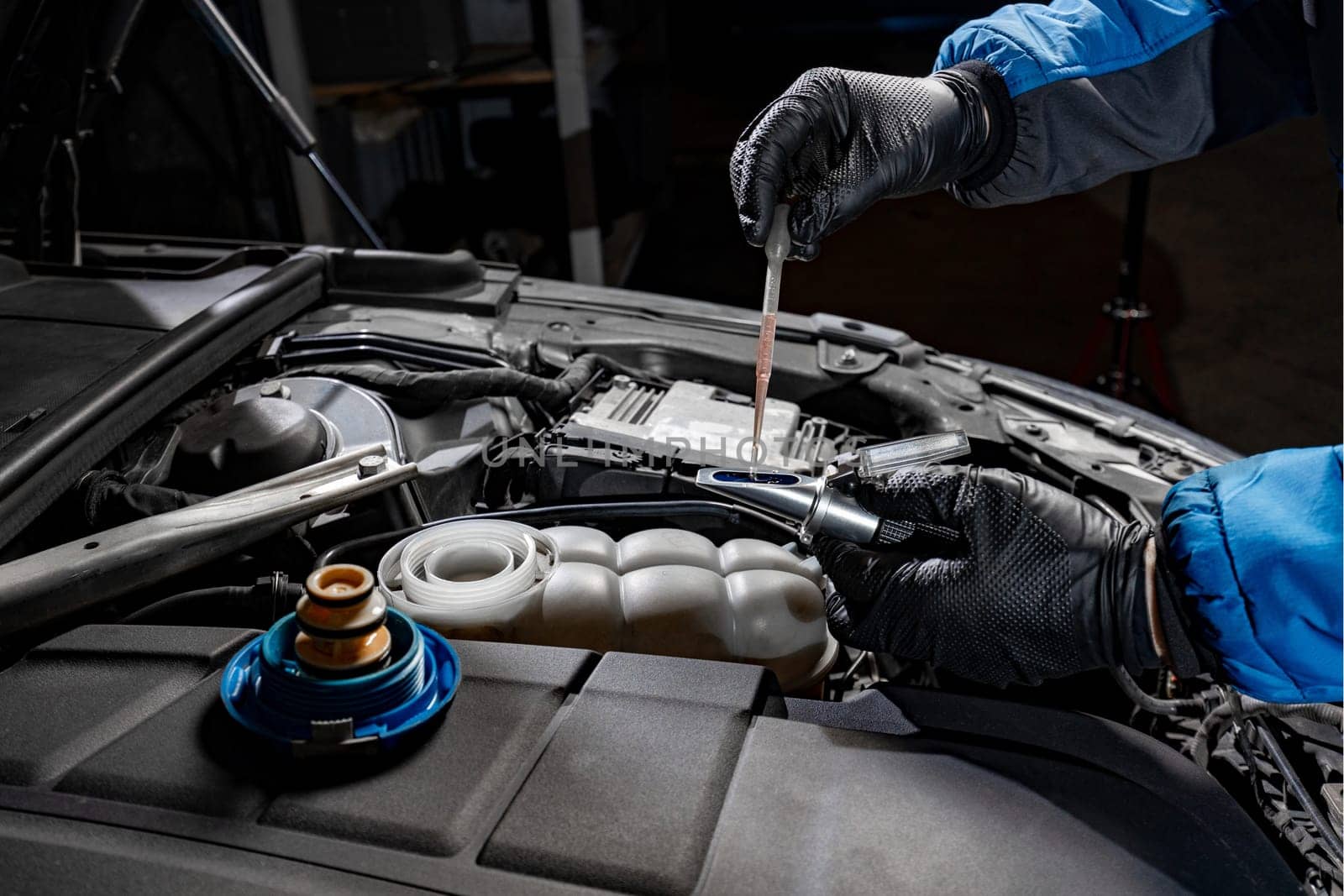 Witness the precision of a mechanic's gloved hands as they carefully extract brake fluid from under the hood using a disposable pipette, placing it onto the refractometer lens to verify the brake fluid concentration