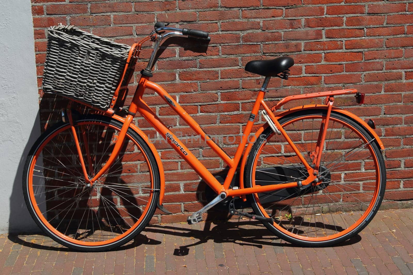 an old orange bicycle stands on a red house wall