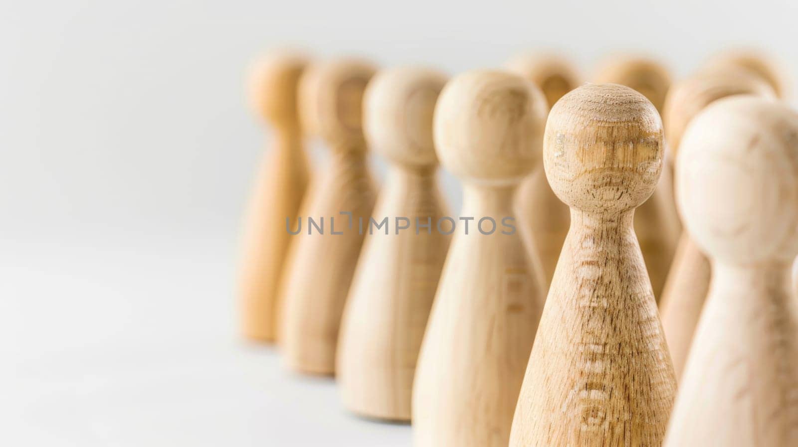 A straight row of wooden pegs is neatly lined up against a plain white background. The pegs are uniformly shaped and spaced, creating a symmetrical and orderly arrangement.