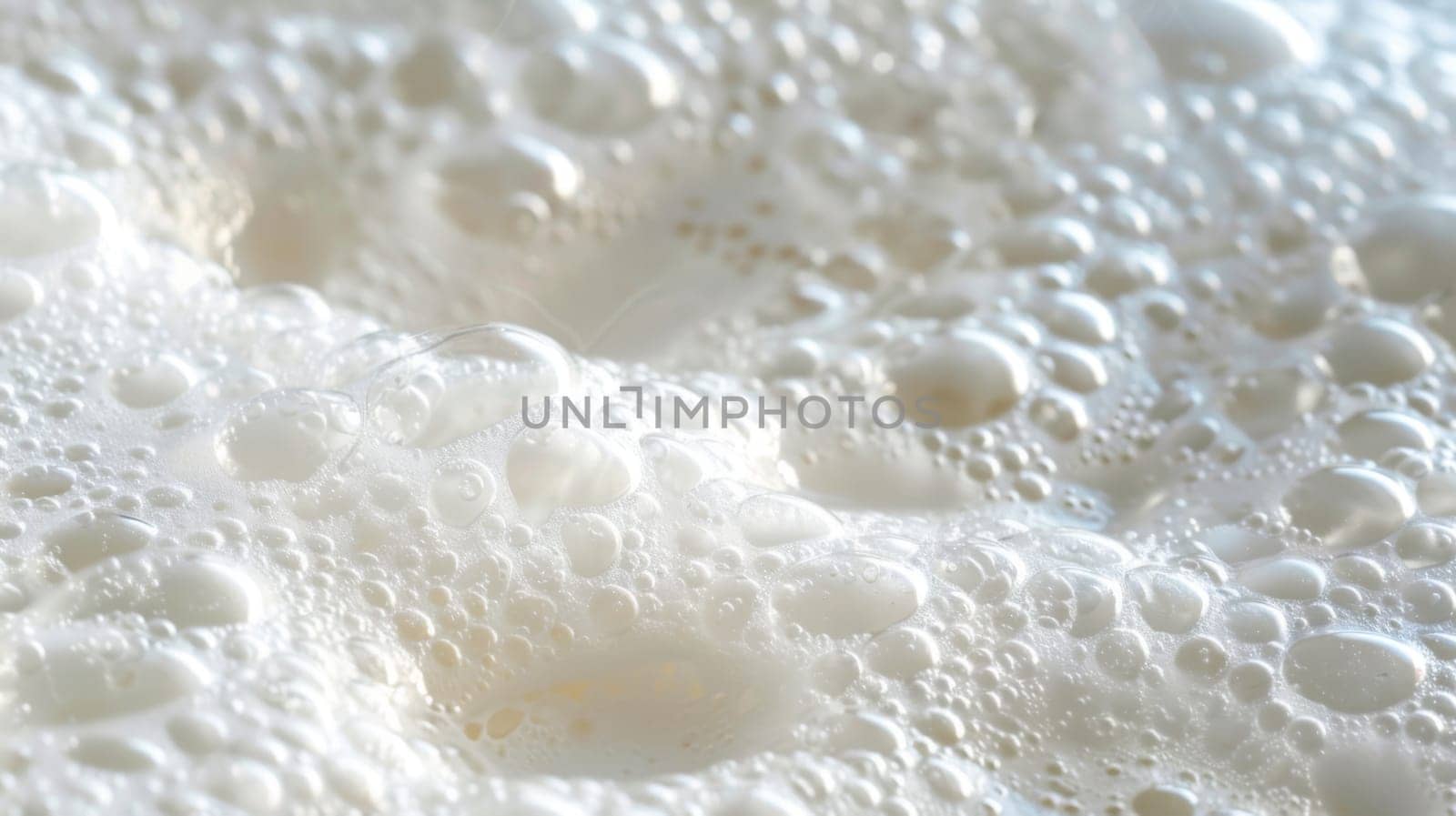Numerous bubbles are shown in extreme close-up on a white surface, each reflecting light and creating a textured pattern. The bubbles vary in size and shape, some merging into larger ones while others pop and disappear.