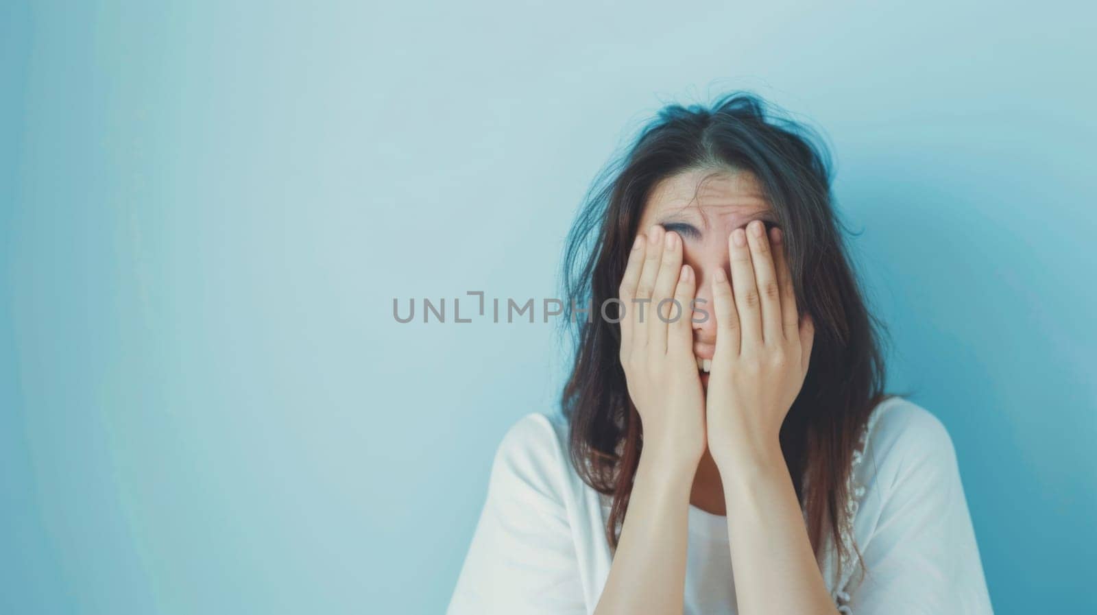 A woman is shown with her hands covering her face, hiding her expression. She appears to be in distress, anxiety, or frustration, seeking solace or privacy.