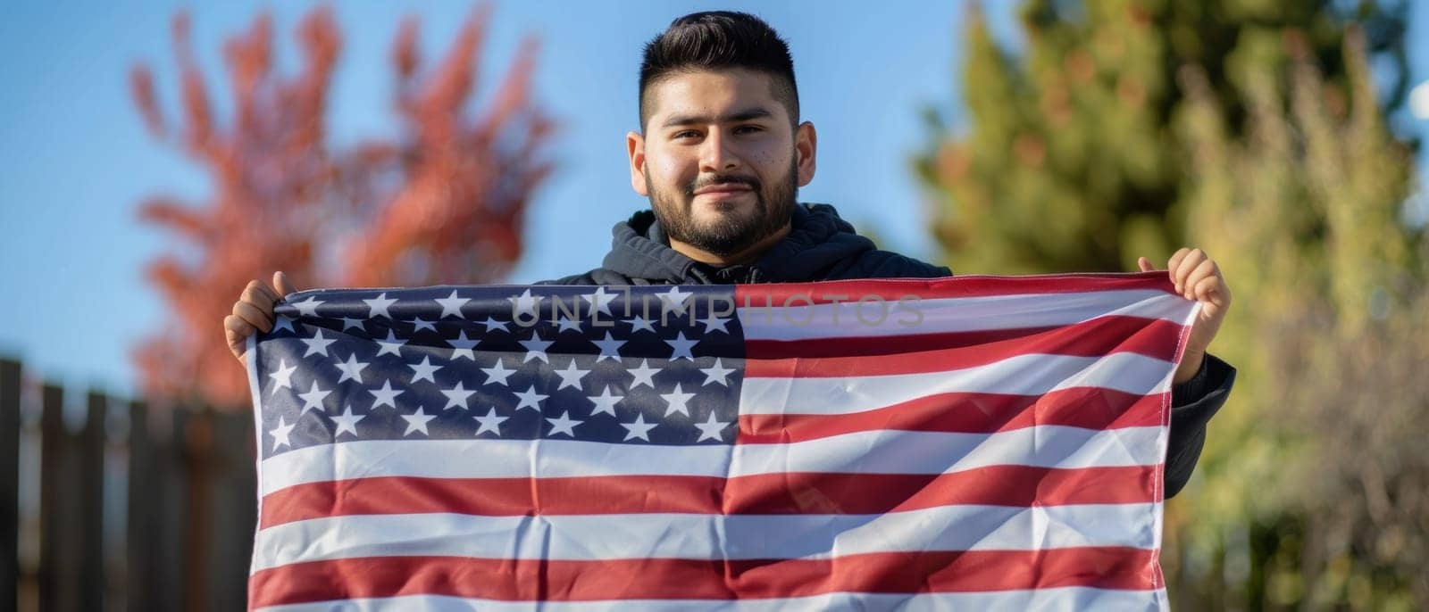 A proud young man holds the American flag with autumn foliage in the background, symbolizing patriotism and change