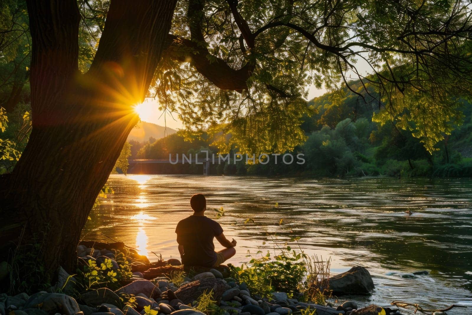 Peaceful image of a person meditating by a riverbank at sunset with trees in the background