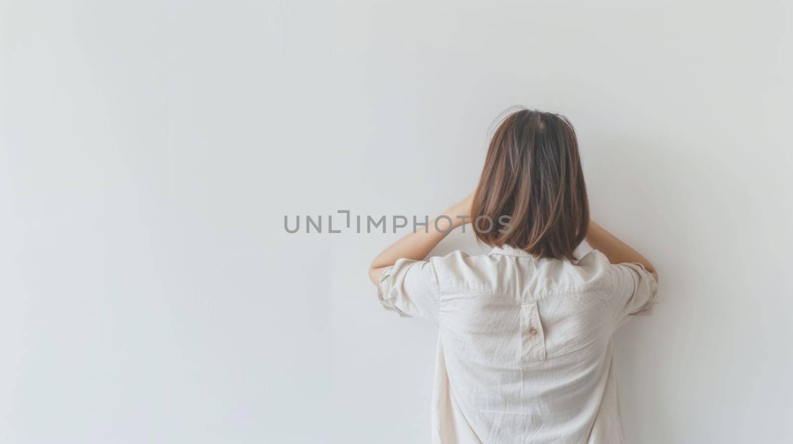 A woman is standing with her back to the camera against a wall. She appears to be still and contemplative in the urban environment.
