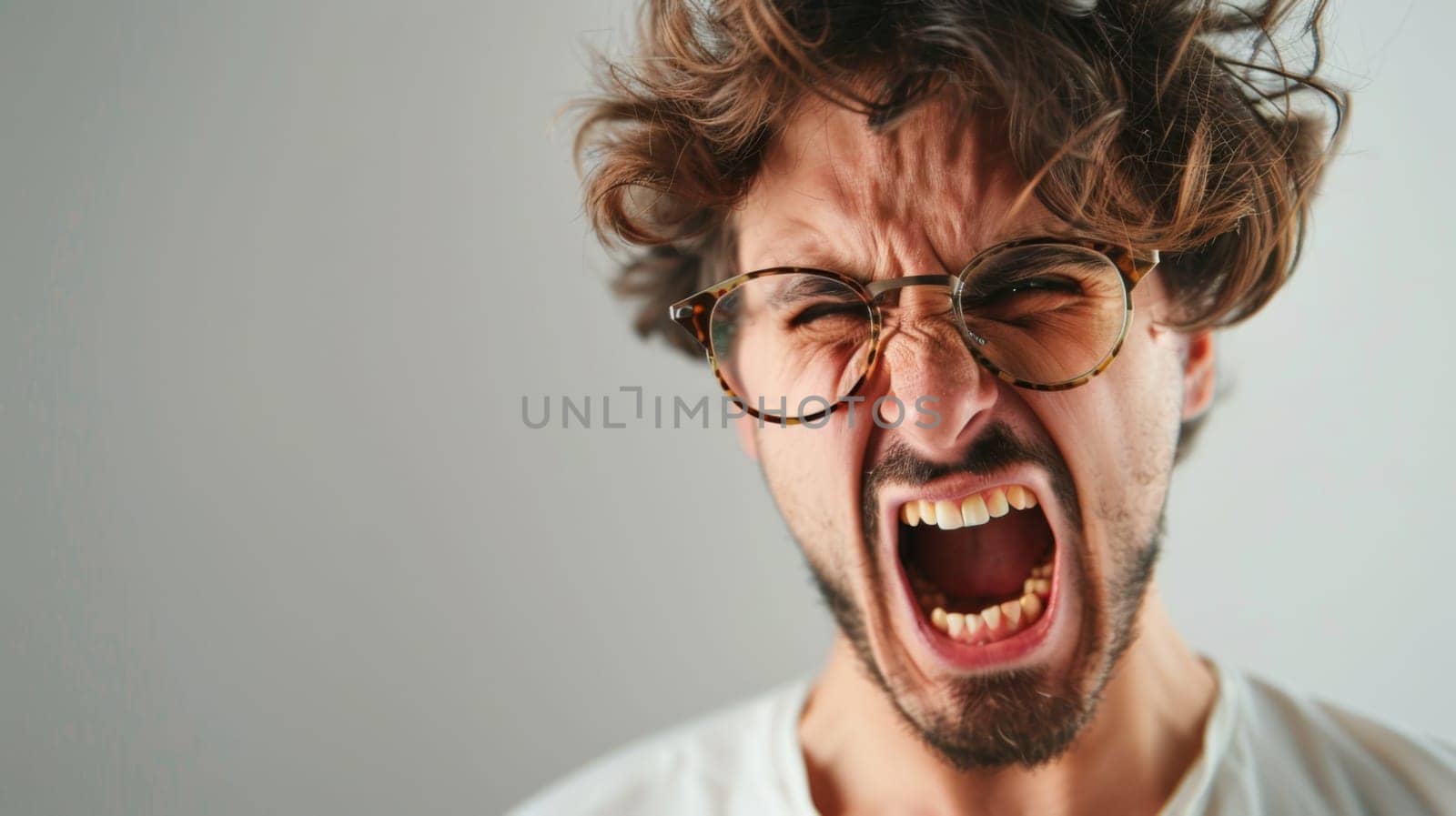 A man with glasses and a beard is visibly enraged, screaming at the top of his lungs. His facial expression shows intense anger and frustration as he vocalizes his emotions loudly.