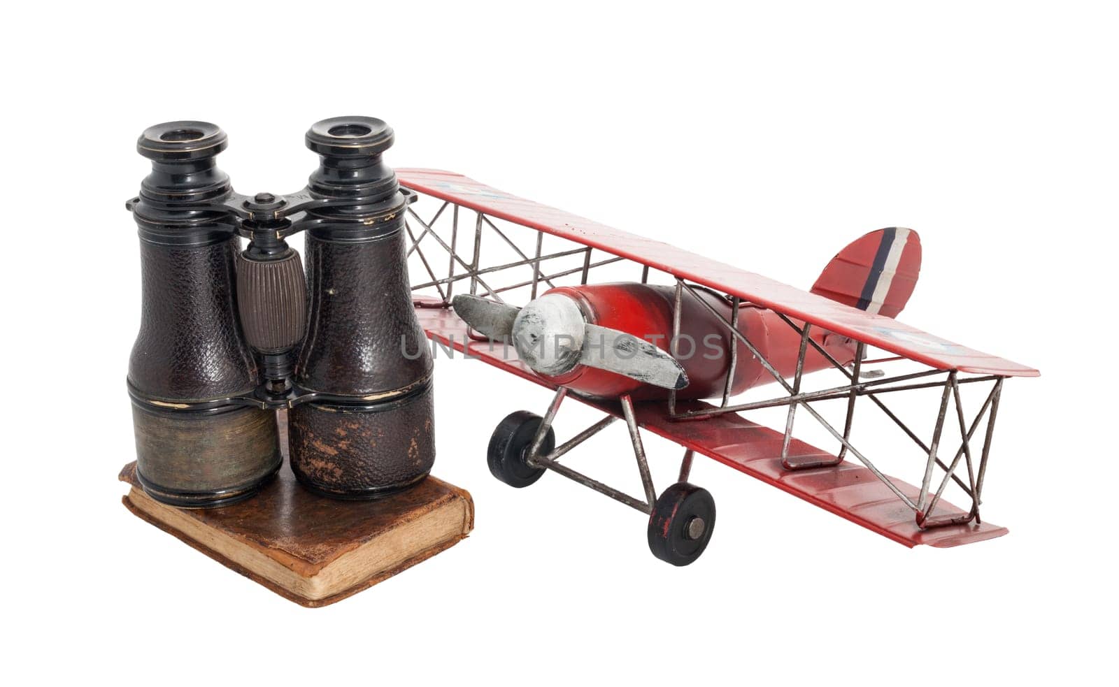 Old time-worn objects full of poetry, fun and adventure: a tin airplane, an old book with a leather cover and binoculars on top. Ready for adventurous travels!