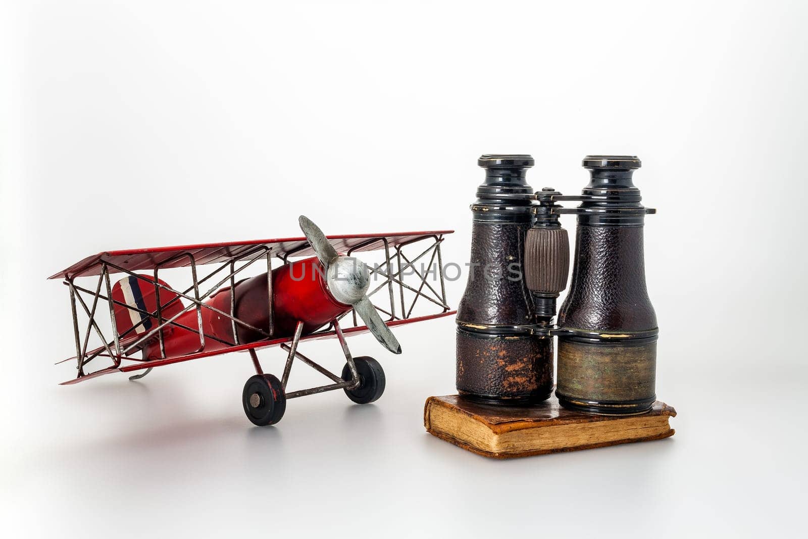 Antiques including film gear, tin aeroplanes, aged binoculars, and diaries on a white canvas, symbolizing age-old quests and revelations