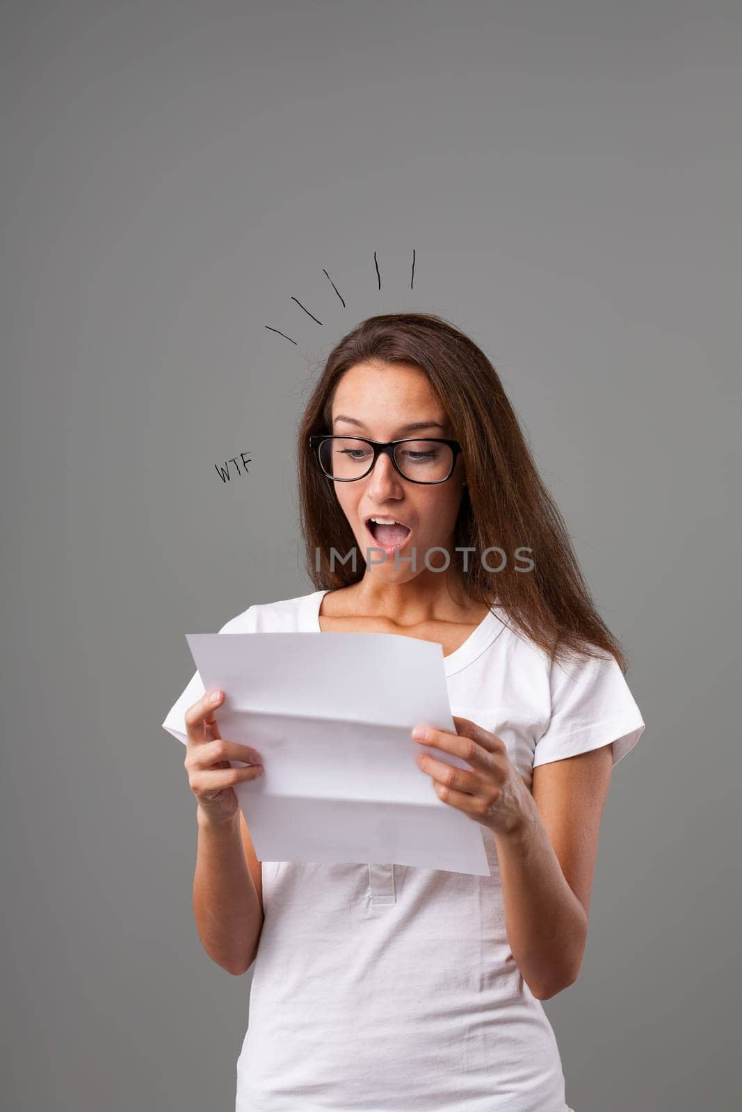Emotional portrait of a young woman isolated on a neutral background. She's shocked, mouth agape at the surprising news she's reading in a letter. A formal written communication has caught her in a WT