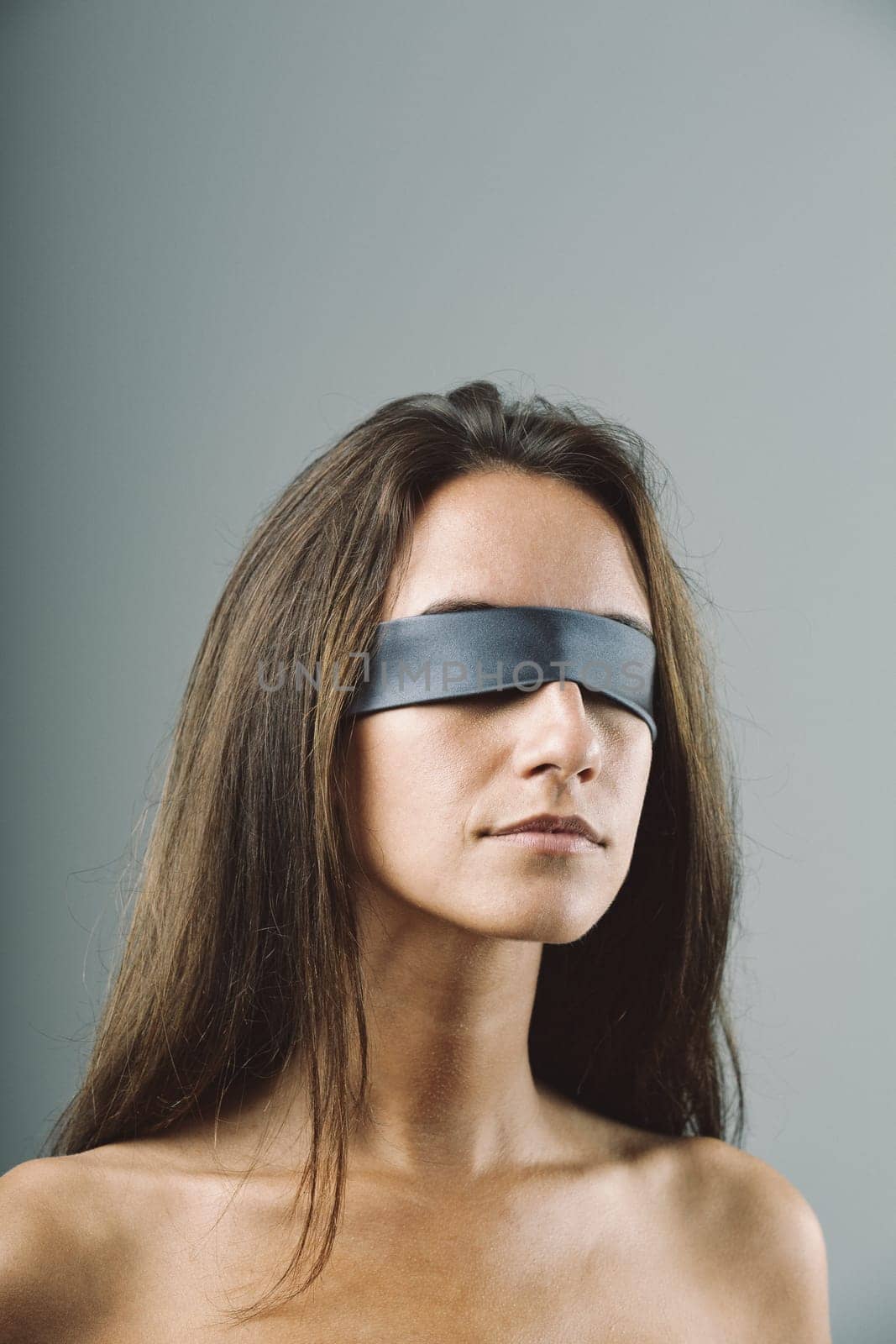 Defenseless, blindfolded woman, inexpressive and silent. Lips closed, no fear conveyed. Possibly awaiting unique sexual practice or in danger. Concept of unexpected and invisible anticipation