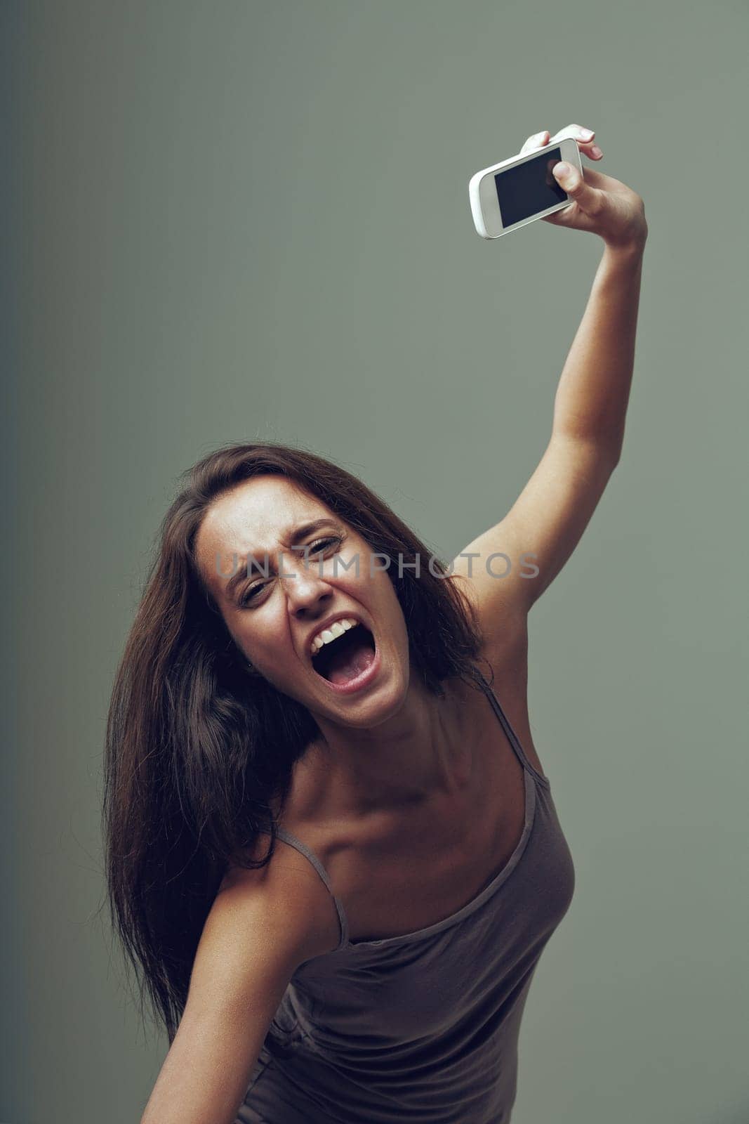 Angry girl throws her cellphone with rage. Emotional portrait of a young woman isolated on a neutral background. She thinks, 'I'm fed up with this smartphone and internet not working!' as she screams