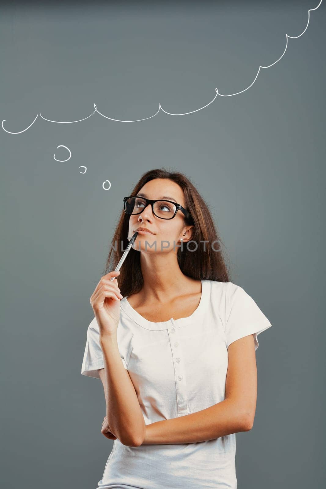 State of mind portrait of a young woman isolated on a neutral background. Thoughtful girl looks up, imagining, inventing. Arms crossed, pen to mouth with one hand. Perhaps a revolutionary idea. Long b