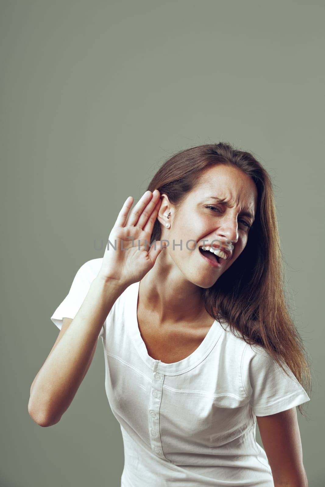 'What did you say? I can't hear you!' seems to be the meaning behind young woman's hand to ear gesture and annoyed expression. Beautiful, slim, long-haired, possibly sarcastic