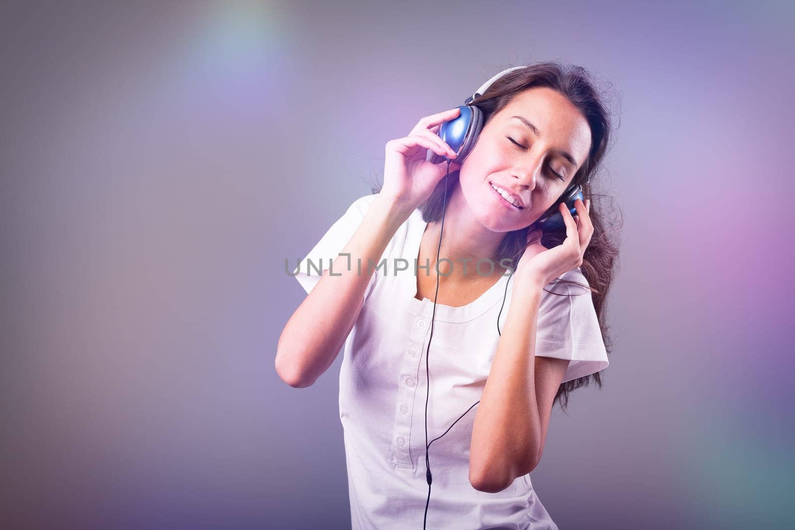 Blue headphones-clad girl dances, sings to music amidst dazzling, fast-paced party lights. Evident joy, happiness, and amusement on the face of slim, long-haired young lady