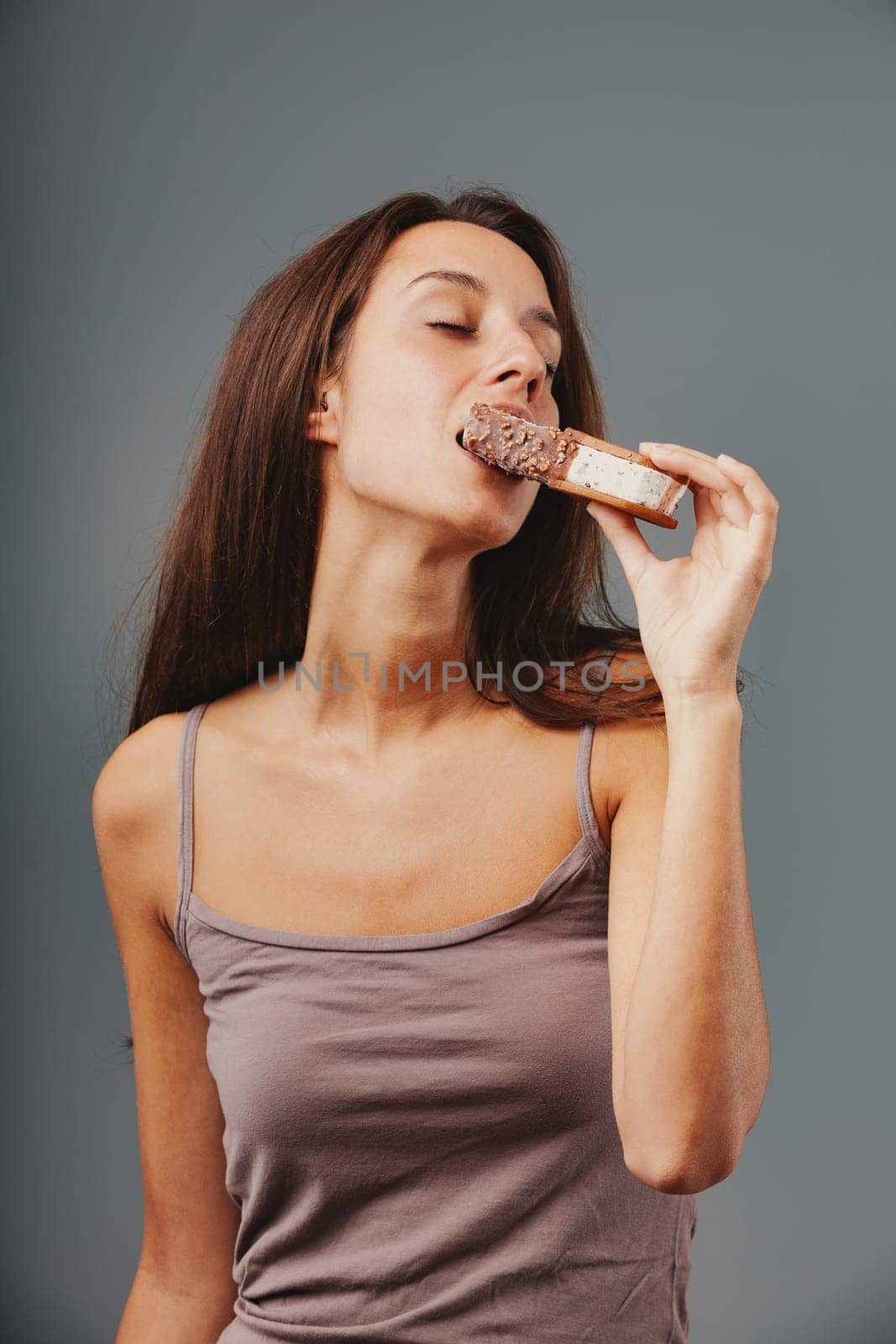 Attractive slim woman indulgently bites chocolate hazelnut ice cream cookie. Immersed in sensual pleasure, her sweet tooth dominates. Unrivaled joy from food and dessert