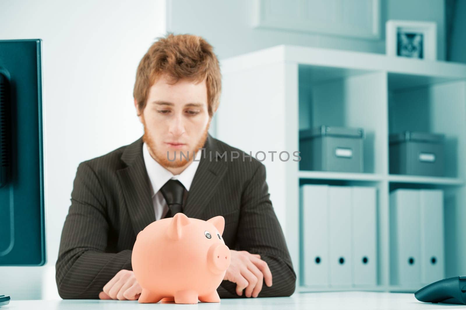 Concept of savings and expenses in business. A young man in a suit looks dejectedly at a piggy bank. Are we bankrupt? Are we about to go bankrupt? Where will we get the money? he wonders.