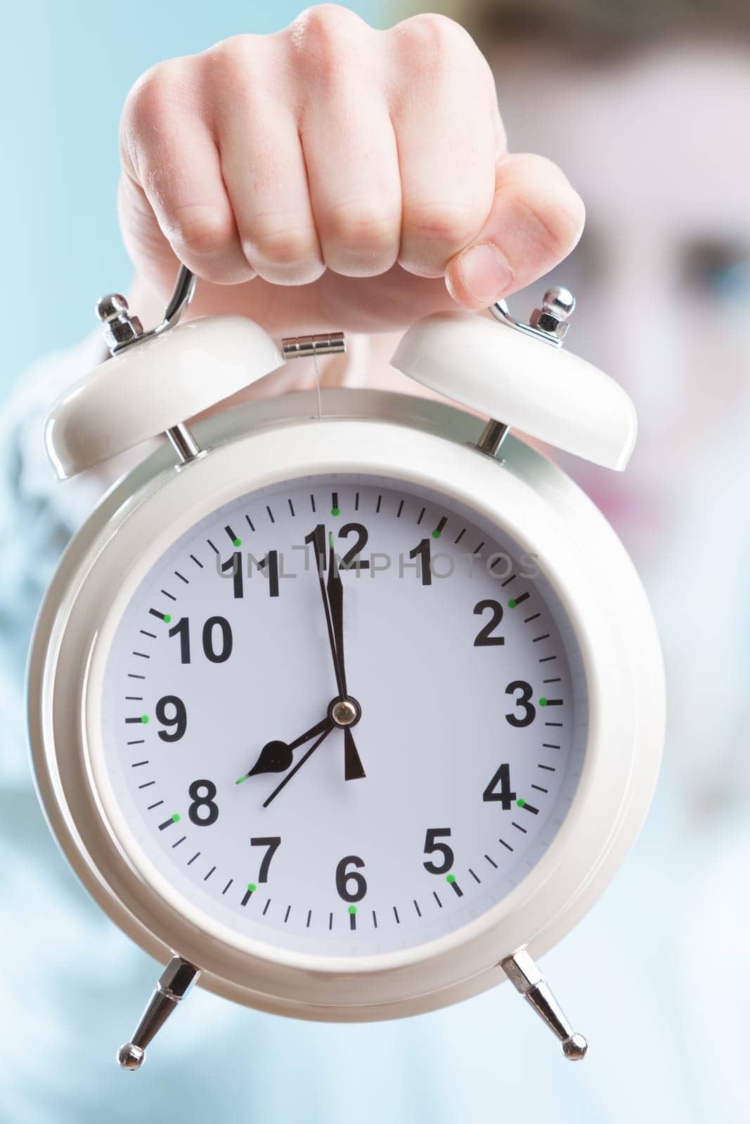 An in-focus hand extending a large alarm clock against a blurry office background. In business, time is money, and deadlines are just around the corner