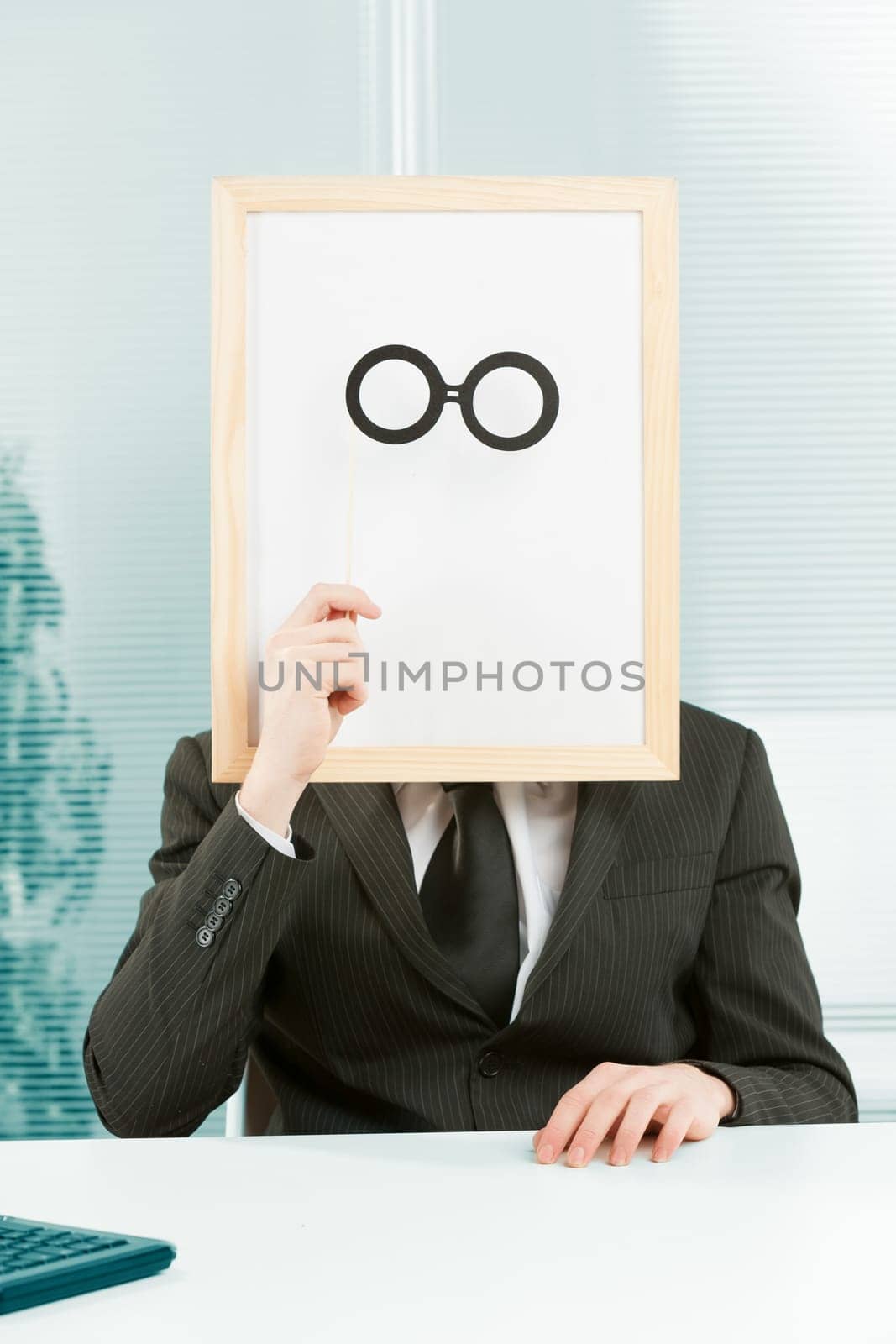 Man with framed sign head in an office. In front of the fake head made of signboard he also places cardboard glasses to complete a disguise that YOU can customize graphically.