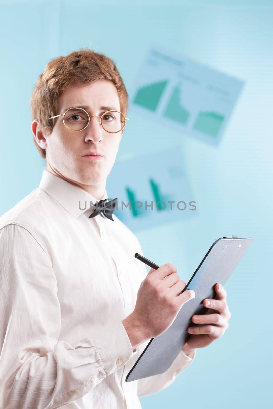 A young man in a dated office suit, perhaps a subservient accountant, with a notepad, white shirt and bowtie, gazes sadly against a generic, blurred office backdrop
