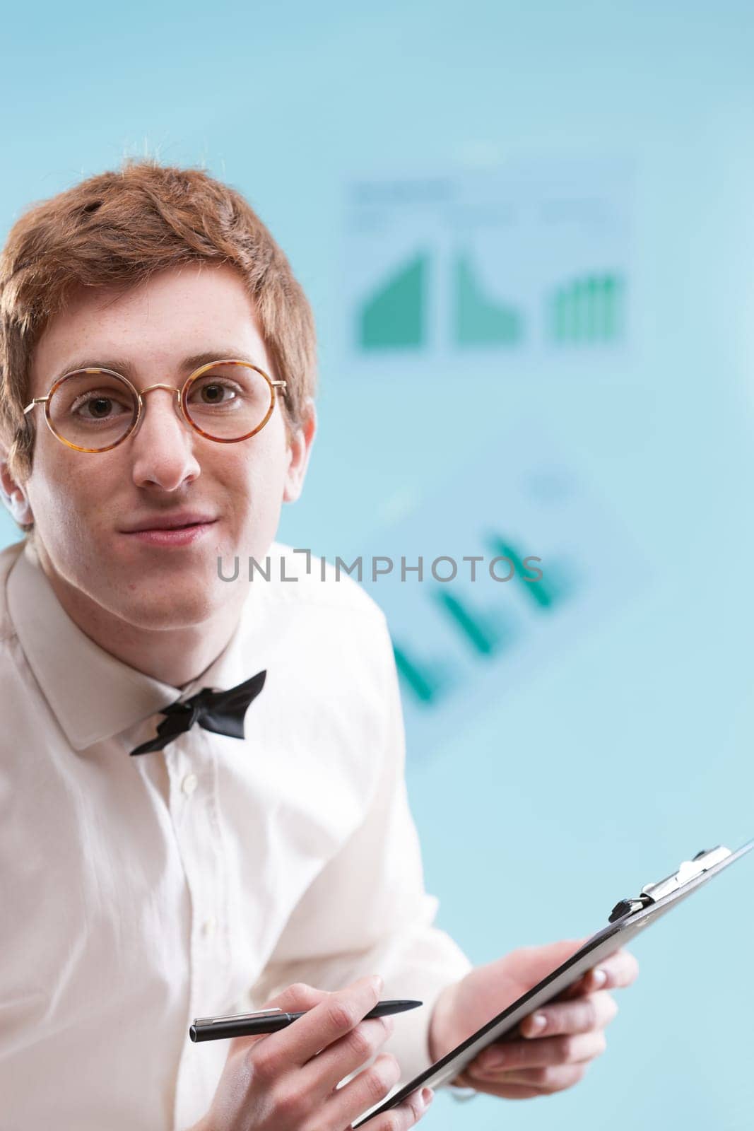 In focus, a young man with a nerdy, subservient vibe, wears a dated office suit and holds a notepad. His white shirt, bowtie, and sad gaze hint at an accountant's life