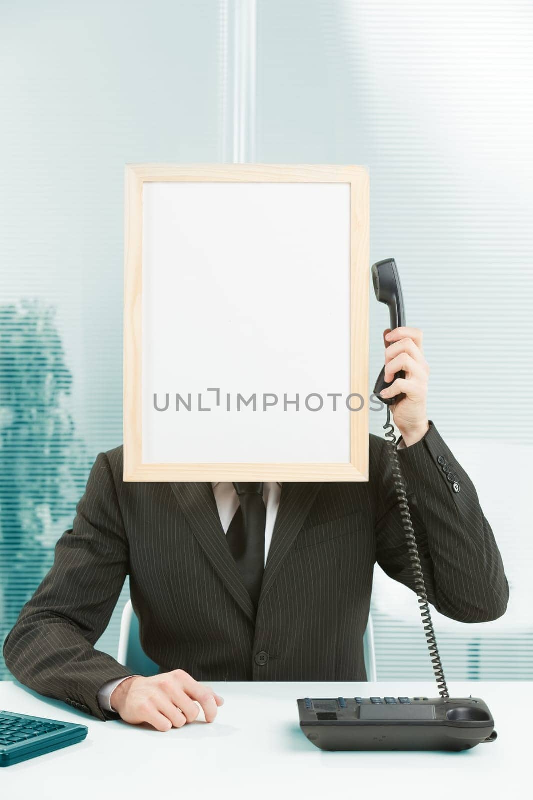 Man with framed sign head in an office answers phone. He has his arm raised with the handset in his hand, which he pulls over to the sign-head to listen. Concept of call center and customer care.