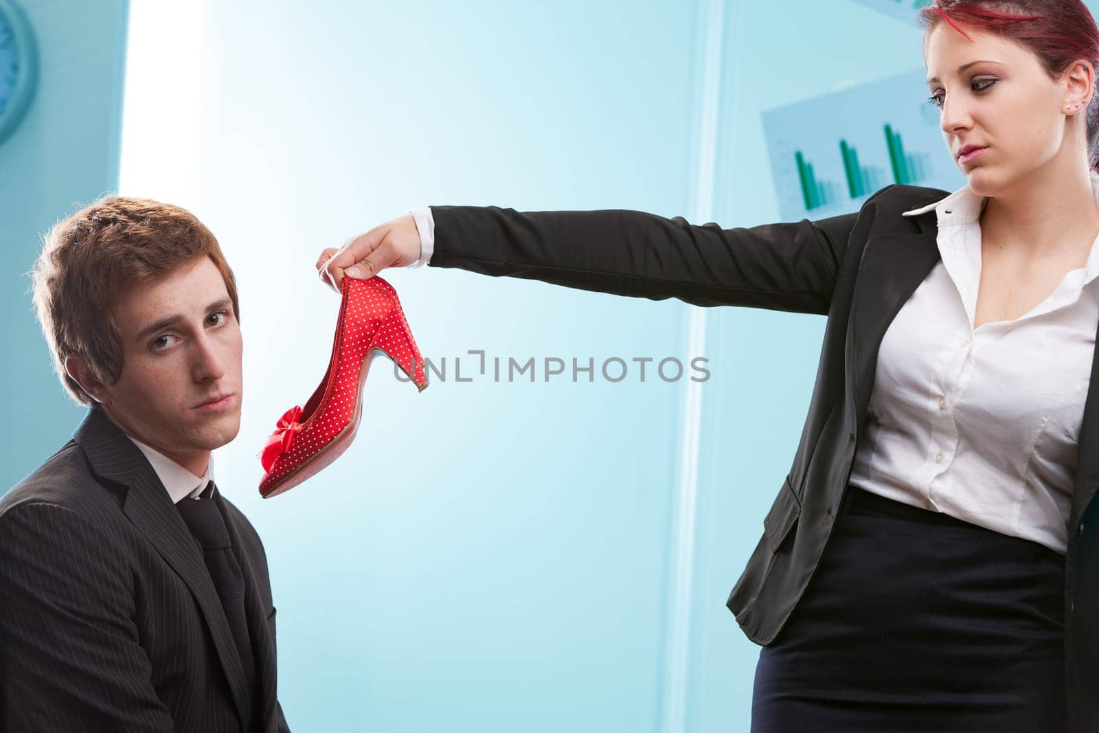 Man offered heels by woman: her stand against fashion serving male tastes. Turning tables on traditional dominance, she reflects past actions
