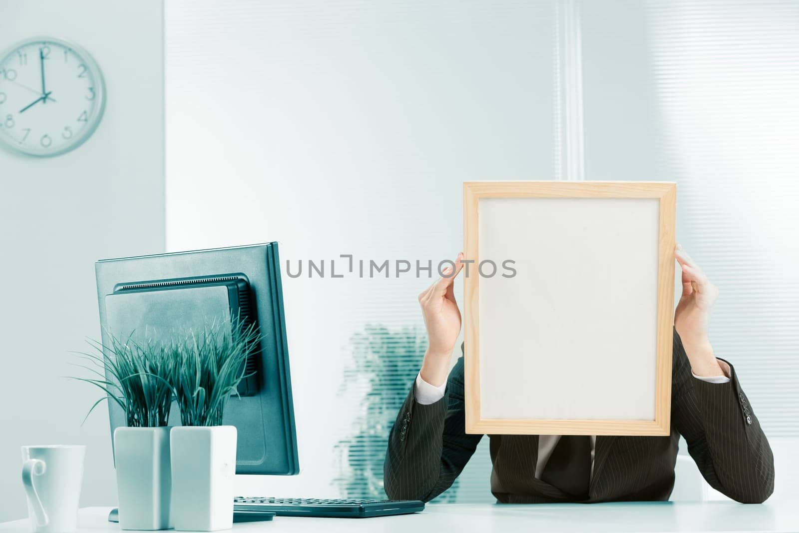 Office workplace, a sign-headed man framed in light wood holds the sign-head with his hands. Either he is very worried or he is pressing his temples with a headache. A PC monitor is visible on the des