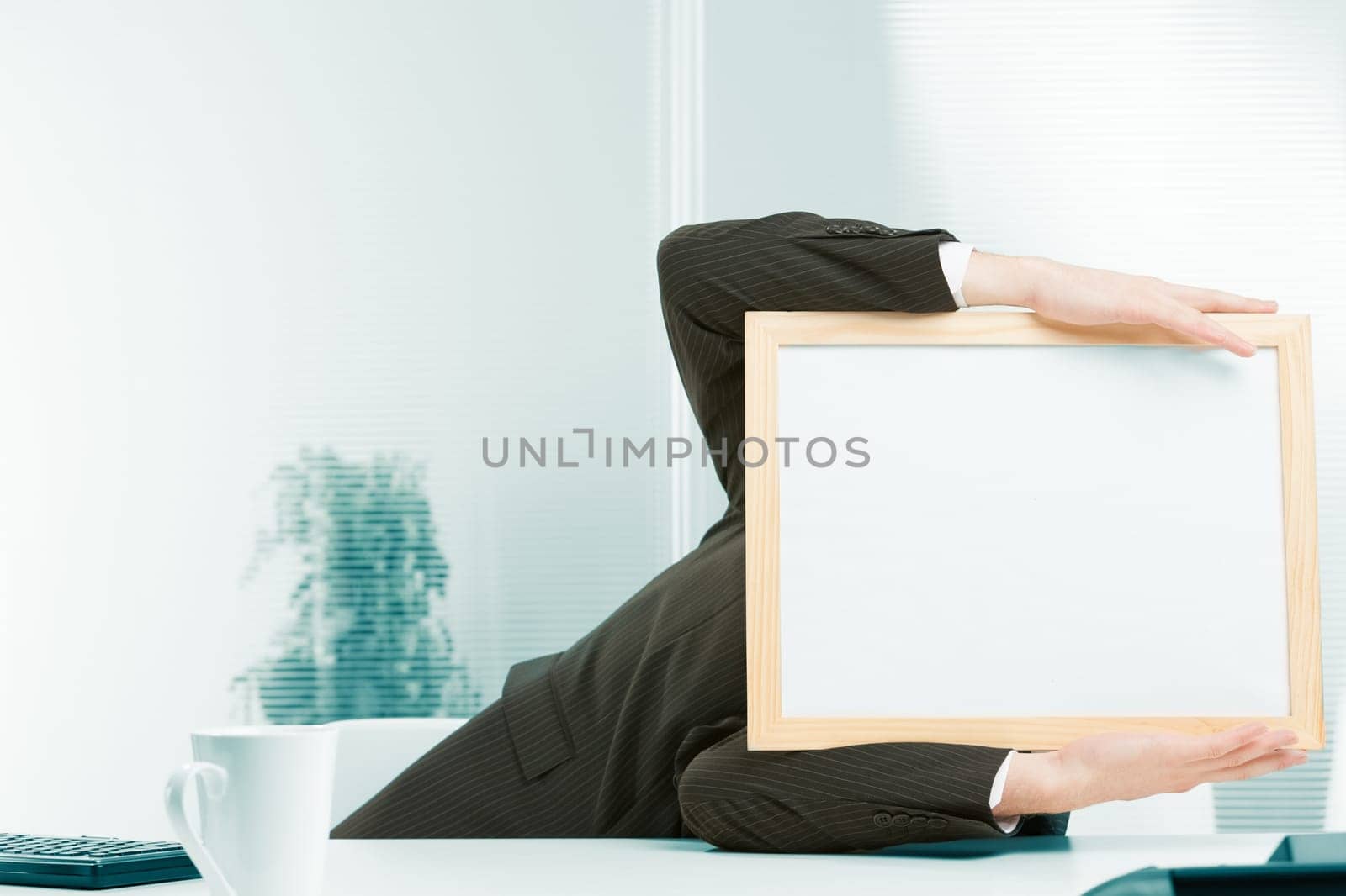 Office workplace, a sign-headed man framed in light-colored wood leans to the side from a fainting spell, a shock from strong negative news. He holds up the sign-head perhaps also from a headache.