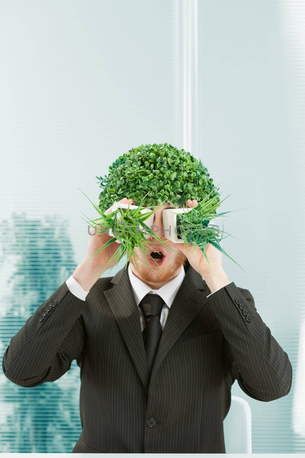 A clerk in an office makes a stunned face in a surreal mood. He has a bush for hair and looks through two pots of grass side by side as if through binoculars. 80s style in the mimicry. Black pinstripe